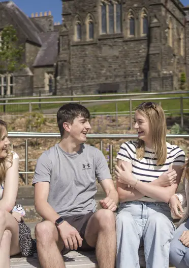 Students sat on a wall outside of their university campus